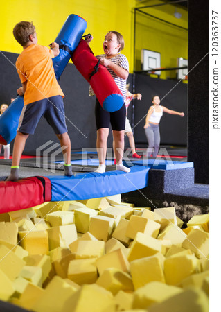 Preteen girl fighting by pugil stick with boy on inflatable beam Preteen girl fighting by pugil stick with boy on inflatable beam 120363737