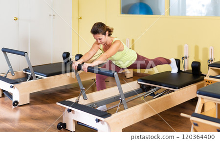 Young woman doing pilates exercises with reformer bed 120364400