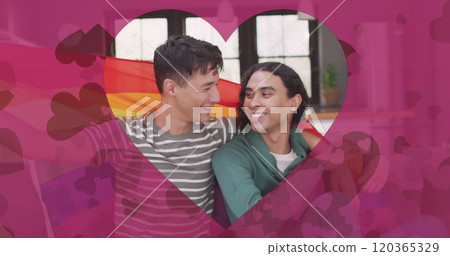 Image of heart cut out over happy diverse gay male couple embracing in rainbow flag 120365329