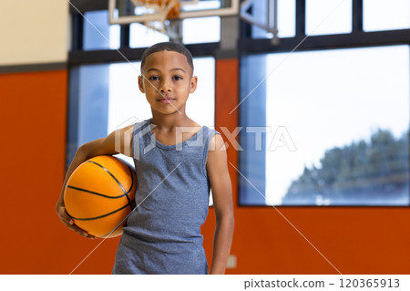 In school gym, boy holding basketball, ready for practice or game, copy space 120365913