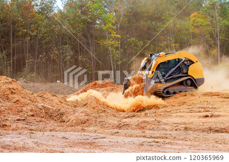 Powerful bulldozer is actively pushing dirt debris at construction site surrounded by trees dust clouds billow into air as land is being prepared for development. Powerful bulldozer is actively pushing dirt debris at construction site surrounded by trees dust clouds billow into air as land is being prepared for development. 120365969