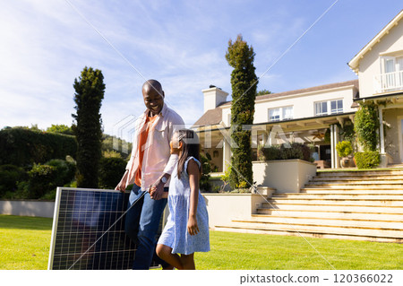 Carrying solar panel, father and daughter smiling and walking in front yard Carrying solar panel, father and daughter smiling and walking in front yard 120366022