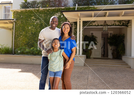 Smiling family of three with daughter standing together outside their home, enjoying time 120366052