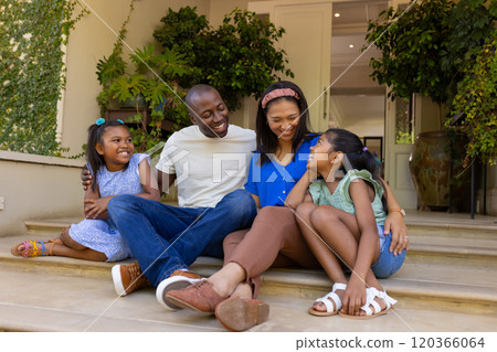 Sitting on steps, happy family of four with daughters enjoying time together outdoors 120366064