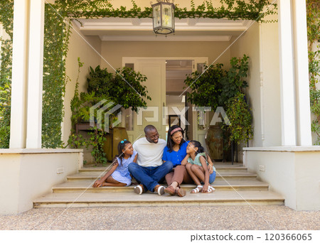 Sitting on porch steps, family of four with daughters enjoying quality time together 120366065