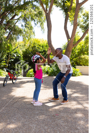 High-fiving, father and daughter bonding outdoors with bicycle in background 120366101