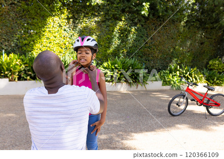 Adjusting bike helmet, father ensuring daughter's safety before cycling outdoors Adjusting bike helmet, father ensuring daughter's safety before cycling outdoors 120366109