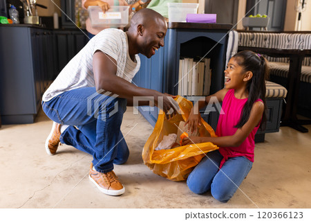 Father and daughter cleaning kitchen together, putting trash in yellow bag 120366123
