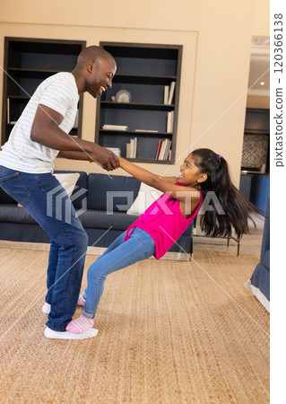 Father and daughter playing together, holding hands and smiling in living room 120366138