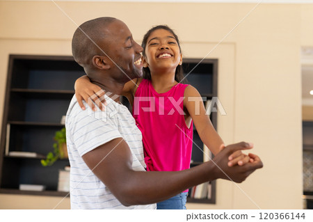 Father and daughter dancing together, smiling and enjoying family time at home 120366144