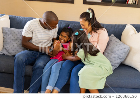 Family of four sitting on couch, parents tickling and playing with children 120366150