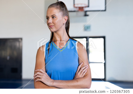 In school gym, woman in basketball jersey standing with arms crossed In school gym, woman in basketball jersey standing with arms crossed 120367305