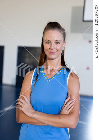 In gym, female basketball player in blue jersey standing with arms crossed In gym, female basketball player in blue jersey standing with arms crossed 120367307