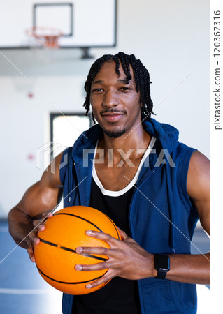 Holding basketball, african american man smiling confidently in indoor school basketball court 120367316