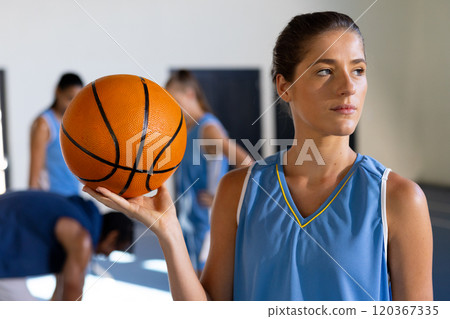 Holding basketball, female basketball player in sports uniform looking away in gym 120367335