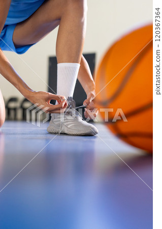 Tying shoelaces, female basketball player preparing for game on court 120367364