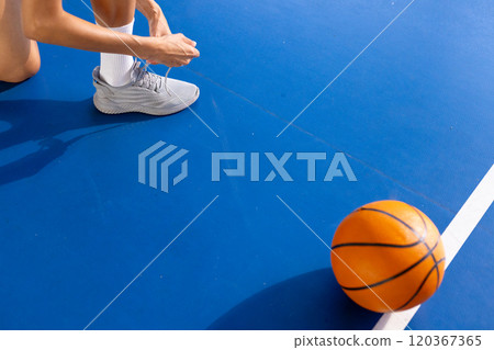 Tying shoelaces on basketball court, woman preparing for game with ball nearby, copy space 120367365