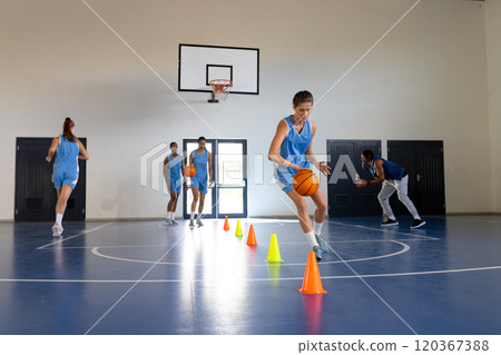 Dribbling basketball around cones, female athlete training in school gym, copy space Dribbling basketball around cones, female athlete training in school gym, copy space 120367388