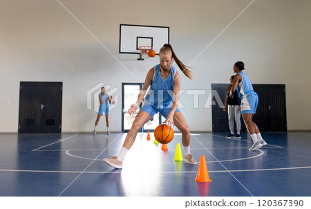 Dribbling basketball around cones, female basketball player practicing in gym Dribbling basketball around cones, female basketball player practicing in gym 120367390