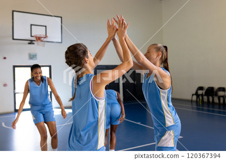 Celebrating victory in school gym, female basketball players high-fiving teammates 120367394