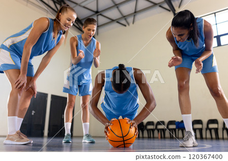 Basketball team encouraging teammate holding ball during practice in gym 120367400
