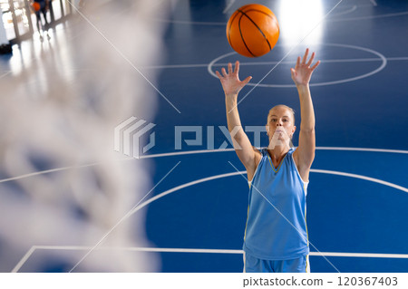 Playing basketball, woman shooting ball towards hoop on indoor court, copy space 120367403