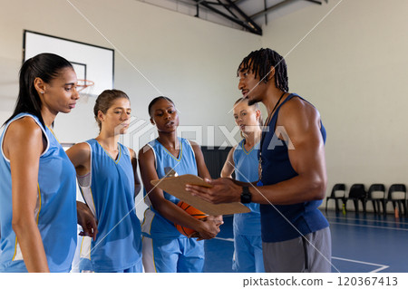 Basketball male coach discussing strategy with female team players in gym 120367413