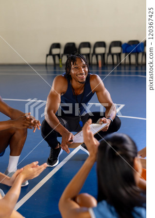 Coaching basketball team, man holding clipboard and smiling at players 120367425