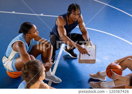 Basketball male coach discussing strategy with female players on court during practice Basketball male coach discussing strategy with female players on court during practice 120367426