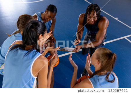 Basketball male coach discussing strategy with female team players on court Basketball male coach discussing strategy with female team players on court 120367431