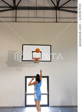 Playing basketball, woman shooting ball towards hoop in indoor court 120367433