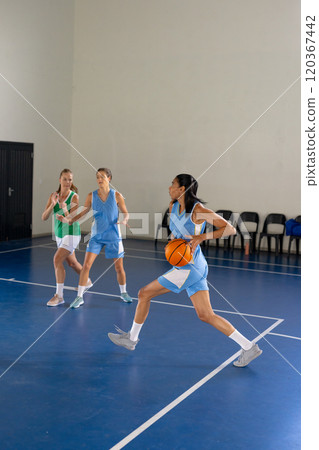 Playing basketball, female african american man dribbling ball while teammates defend in gym 120367442