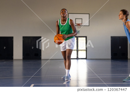 Playing basketball, woman in green jersey preparing to shoot ball in gym 120367447