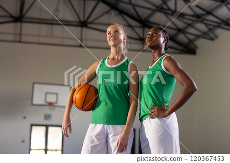 Holding basketball, two female basketball players posing confidently in gym Holding basketball, two female basketball players posing confidently in gym 120367453