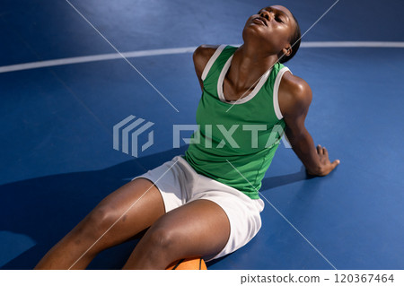 Resting on basketball court, female basketball player in green jersey relaxing Resting on basketball court, female basketball player in green jersey relaxing 120367464