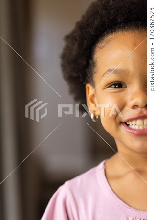 Smiling girl with curly hair wearing pink shirt, showing happiness at home, copy space 120367523