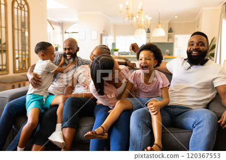 Laughing and playing, multi-generational family sitting together on living room sofa 120367553