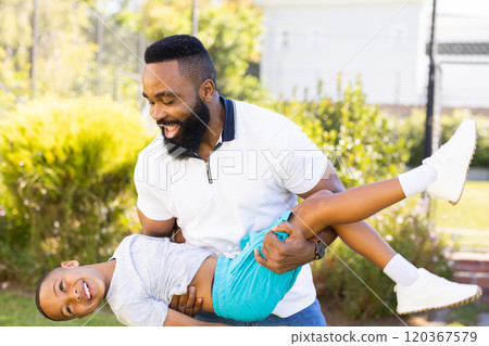 Playing together, father holding and swinging son outdoors, enjoying family time 120367579