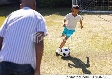 Playing soccer, grandson dribbling ball on field with grandfather watching attentively 120367615