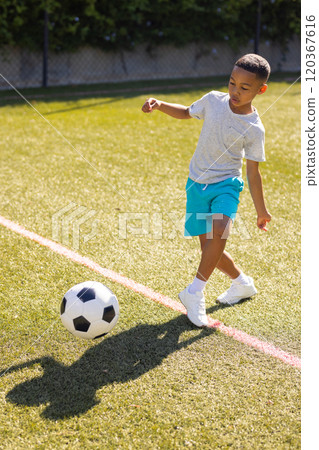 Playing soccer, young boy kicking ball on grassy field outdoors 120367616