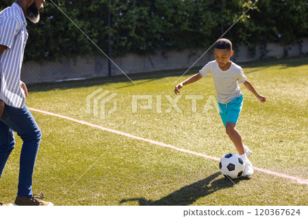 Playing soccer on field, young boy dribbling ball with grandson supervising nearby, copy space 120367624