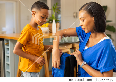 Packing school backpack, mother helping young son in kitchen before school Packing school backpack, mother helping young son in kitchen before school 120367649