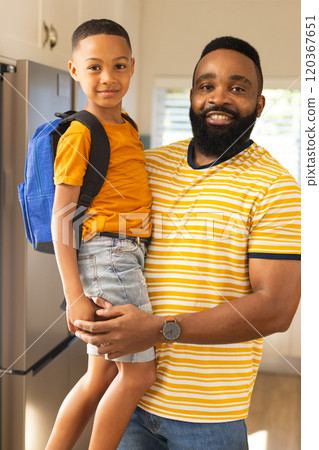 Father holding son with backpack, smiling and ready for school in kitchen Father holding son with backpack, smiling and ready for school in kitchen 120367651