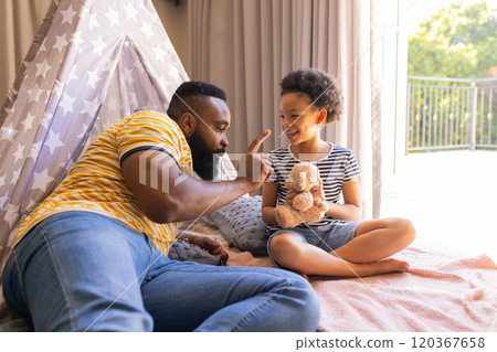 Playing with stuffed animal, father and daughter bonding in cozy home setting, in teepee Playing with stuffed animal, father and daughter bonding in cozy home setting, in teepee 120367658