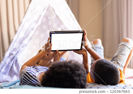 brother and sister lying on bed using tablet, enjoying leisure time at home, copy space, in teepee 120367663