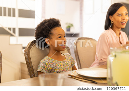 Smiling girl sitting at dining table with family, enjoying quality time together 120367721