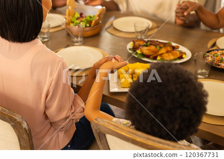 Holding hands, multigenerational family sitting at dining table with food, preparing to eat together Holding hands, multigenerational family sitting at dining table with food, preparing to eat together 120367731
