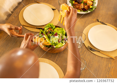 Serving fresh salad at family dinner table, hands preparing meal together Serving fresh salad at family dinner table, hands preparing meal together 120367732