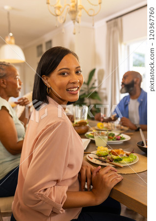 Smiling woman enjoying meal with family at dining table, sharing quality time 120367760