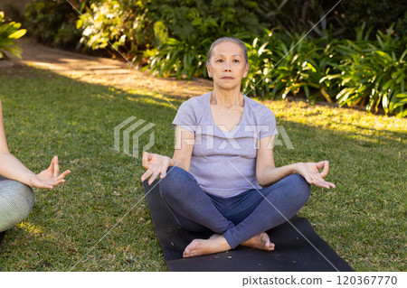 Meditating on yoga mat, senior asian woman practicing mindfulness in outdoor garden setting Meditating on yoga mat, senior asian woman practicing mindfulness in outdoor garden setting 120367770